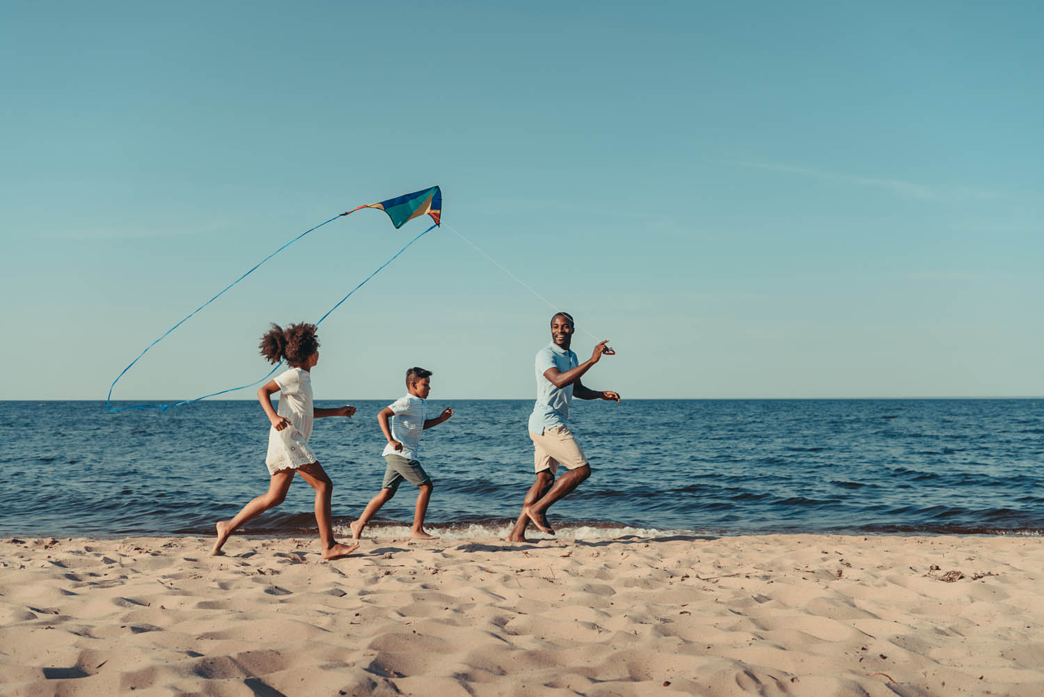 father and kids playing with kite on beach